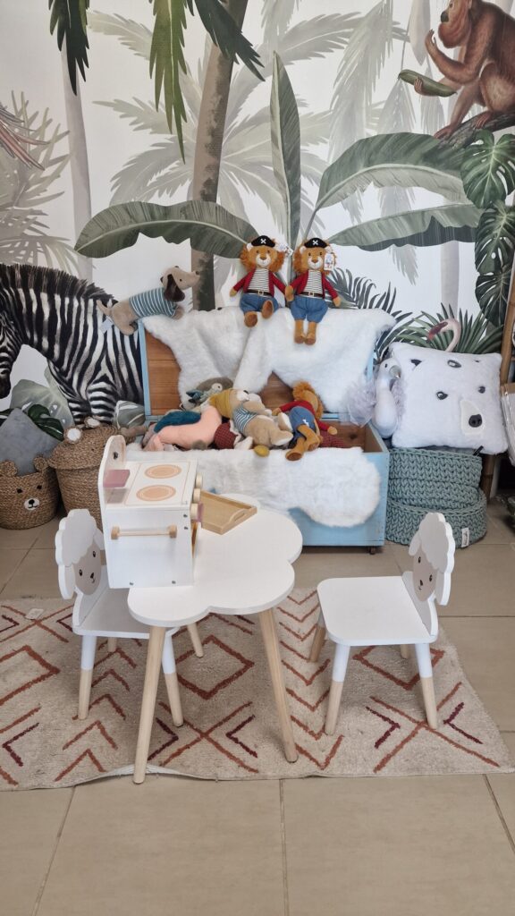 Espace enfant dans la boutique Merci Cheri à Auterive, avec une petite table et des chaises décorées de motifs d'animaux, entourées de peluches et de jouets